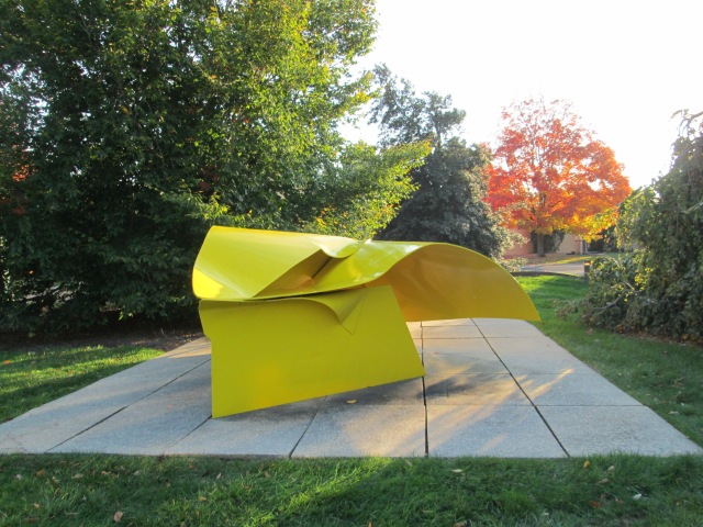 yello abstract swirly sculpture surrounded by trees and grass